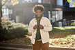 Cool smiling positive young African American guy model standing at big city sunny street. Stylish ethnic hipster generation z teen feeling happy looking at camera outdoors in park, portrait.