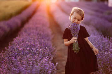 Portrait of a cute girl with a bouquet of lavender flowers in her hands. A child is walking in a field of lavender on sunset. Kid in black dress is having fun on nature on summer holiday vacation.