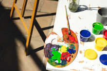 Close Up Of Colorful Paints, Painting Palette And Brushes On Table In Garden