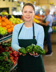 Wall Mural - woman seller offers buyer to choose ripe sweet pepper of green or red color