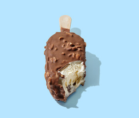 Wall Mural - Bitten chocolate ice cream on a stick blue pastel background