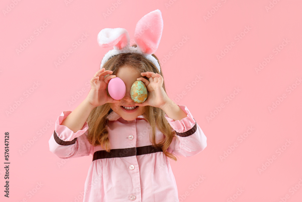 Cute little girl in bunny ears with painted Easter eggs on pink background
