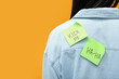 Sticky papers on woman's back against orange background, closeup. April Fools' Day celebration