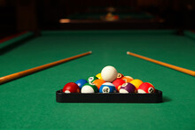 Plastic triangle rack with billiard balls and cues on green table indoors