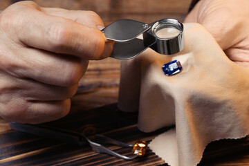 Professional jeweler working with gemstone at wooden table, closeup