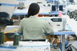 © Serhii - Happy attractive young woman seamstress sitting and sews on sewing machine in studio