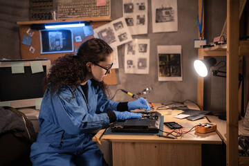 Female technician repairing broken laptop notebook computer with a screwdriver working in retro old repair shop. Hardware developer fixing electronic components. PC technology