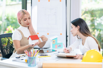 Concept of engineering consulting, Two female engineers discussing about model of building together; Two female architects are studying blueprint of building house.