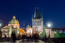 Night View Of Charles Bridge Crowded With Tourists, Old Town Bridge Tower And The Dome Of Charles Bridge Museum Illuminated