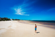 MANDA ISLAND, LAMU, INDIAN OCEAN, KENYA, AFRICA. A Young Woman Walks Down An Empty White Beach Under Bright Blue Sky.