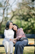 © Nuttapong punna - Happy adult granddaughter and senior grandmother having fun enjoying talk sit with green nature. in park