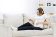 © Andrii - Pregnant woman looking at her stomach on white sofa.