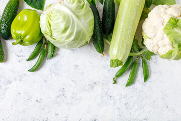 Wall Mural - Border of organic green raw vegetables on white table. Top view of healthy organic food. Copy space