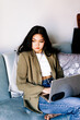 © Jake Jakab - Young asian women listening to music in headphones and dancing energetic and rhythm at couch. Attractive Asian girl looking at the smart phone sitting in the living room spending leisure time at home