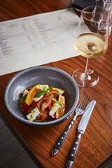 Wall Mural - Dish with salad with tomatoes and cheese and glass of white wine on wooden table in restaurant interior