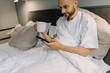 © Igor - Smiling bearded man enjoying coffee in bed while holding phone. This is his morning ritual - starting the day with aromatic coffee and surfing the Internet