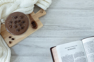 Wall Mural - Romans open holy bible book with cup of coffee and cosy winter scarf on table. Top view. Studying New Testament Scriptures, Christian biblical concept.