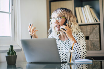 Wall Mural - Adult female entrepreneur at work busy in phone call and explaining solutions to colleagues in remote office workplace. Online job business activity. One businesswoman using device connections