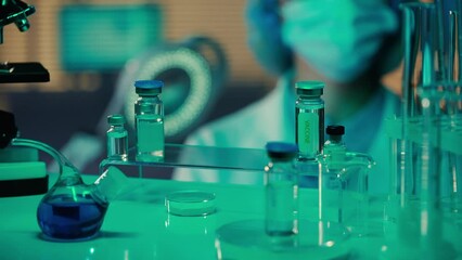 Wall Mural - Woman doctor examines glass vials, flasks, test tubes and enters data into tablet. Female researcher in goggles, mask and gloves in a laboratory or hospital with blue light. Close up.