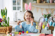© ArtSys - Portrait of cute pretty little girl in blue dress and funny rabbit ears making craft, diy eggs for easter holiday home decoration. Spring colours, bright flowers. Kid's domestic life, hobby, enjoyment