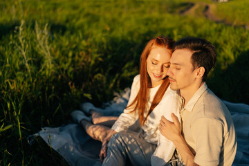 Wall Mural - loving young couple hugging with closed eyes enjoying their time together sitting in field on backgr