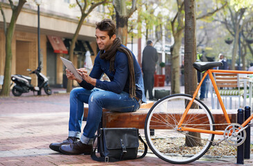 Wall Mural - Relaxed city life moments. Shot of a man using his tablet while taking a break in the city with his bicycle beside him.