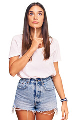 Wall Mural - Young hispanic woman wearing casual white tshirt thinking concentrated about doubt with finger on chin and looking up wondering