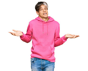 Sticker - Young hispanic man wearing casual pink sweatshirt clueless and confused expression with arms and hands raised. doubt concept.