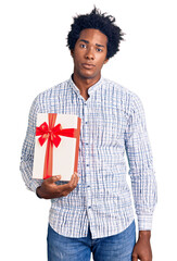 Canvas Print - Handsome african american man with afro hair holding gift thinking attitude and sober expression looking self confident