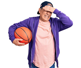 Wall Mural - Senior handsome grey-haired man holding basketball ball stressed and frustrated with hand on head, surprised and angry face