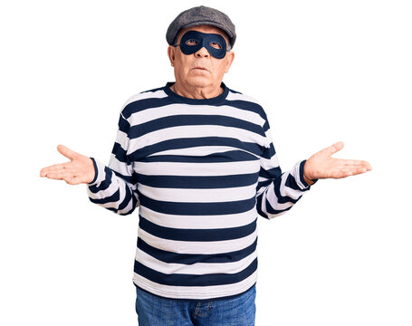 Senior handsome man wearing burglar mask and t-shirt clueless and confused with open arms, no idea concept.