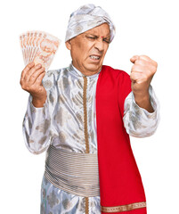 Canvas Print - Senior hispanic man wearing sherwani costume holding 50 indian rupee banknotes annoyed and frustrated shouting with anger, yelling crazy with anger and hand raised