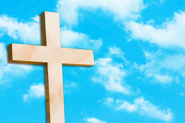 Wooden cross isolated on blue sky. Symbol of christianity with heaven clouds in the background.. Outdoor praying place. Jesus love landscape. Rosary chain hanging.