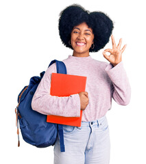 Wall Mural - Young african american girl wearing student backpack holding book doing ok sign with fingers, smiling friendly gesturing excellent symbol