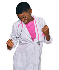 Wall Mural - Young african american woman wearing doctor uniform and stethoscope very happy and excited doing winner gesture with arms raised, smiling and screaming for success. celebration concept.