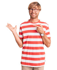 Sticker - Handsome caucasian man with beard wearing casual clothes and glasses amazed and smiling to the camera while presenting with hand and pointing with finger.