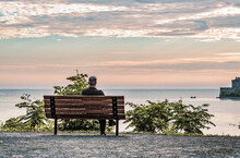 Niagara On The Lake, Ontario, Canada - July 6, 2014.  A Man Sits Ona Bench Overlooking Lake Ontario On A Summer Morning With Dramtic Clouds