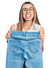 Poster - Hispanic young woman holding slim jeans sticking tongue out happy with funny expression.