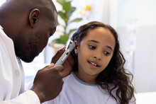 African American Male Doctor Treating Ear Of Biracial Girl In Hospital