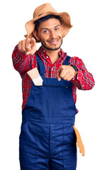 Wall Mural - Handsome latin american young man weaing handyman uniform pointing to you and the camera with fingers, smiling positive and cheerful