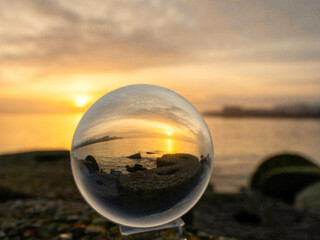 Wall Mural - glass ball on a rough stone by the ocean, sunset sky in the background. warm soft light. selective f