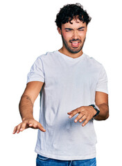 Sticker - Hispanic young man with beard wearing casual white t shirt disgusted expression, displeased and fearful doing disgust face because aversion reaction.