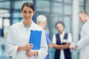 Canvas Print - Your health is our only priority. Portrait of a young female doctor standing in a hospital with colleagues in the background.