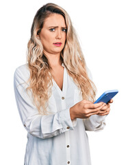 Sticker - Young blonde woman using smartphone clueless and confused expression. doubt concept.