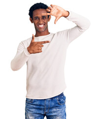 Canvas Print - African handsome man wearing casual winter sweater smiling making frame with hands and fingers with happy face. creativity and photography concept.