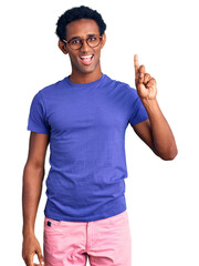 Wall Mural - African handsome man wearing casual clothes and glasses showing and pointing up with finger number one while smiling confident and happy.