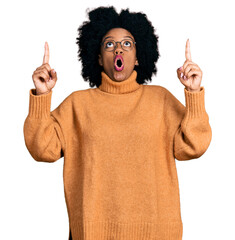 Sticker - Young african american woman wearing casual clothes amazed and surprised looking up and pointing with fingers and raised arms.