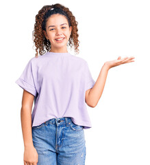 Beautiful kid girl with curly hair wearing casual clothes smiling cheerful presenting and pointing with palm of hand looking at the camera.