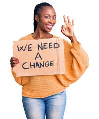 Poster - Young african american woman holding we need a change banner doing ok sign with fingers, smiling friendly gesturing excellent symbol