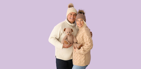 Poster - Happy mature couple in winter clothes and with toy on lilac background